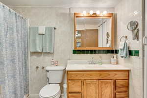 Bathroom featuring toilet, vanity, and tile walls