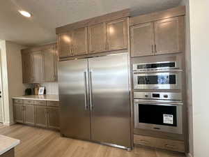 Kitchen featuring tasteful backsplash, light hardwood / wood-style floors, a textured ceiling, and appliances with stainless steel finishes