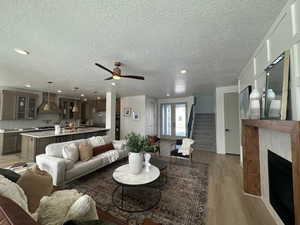 Living room with ceiling fan, a textured ceiling, and light hardwood / wood-style floors