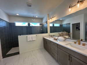 Bathroom featuring tiled shower, vanity, and a textured ceiling