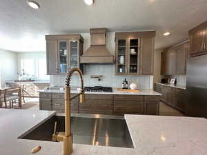 Kitchen with premium range hood, sink, light stone counters, tasteful backsplash, and appliances with stainless steel finishes