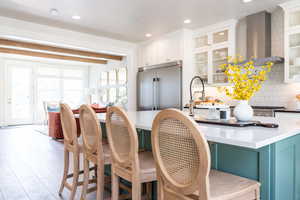 Kitchen with white cabinets, tasteful backsplash, beamed ceiling, high quality fridge, and wall chimney exhaust hood