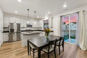 Kitchen with light hardwood / wood-style floors, white cabinets, stainless steel appliances, and pendant lighting