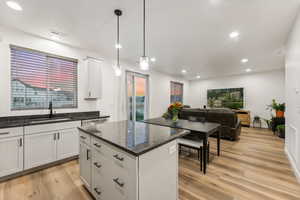 Kitchen with a kitchen island, white cabinetry, pendant lighting, light hardwood / wood-style floors, and sink