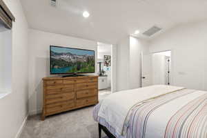 Bedroom with ensuite bathroom, lofted ceiling, and light colored carpet