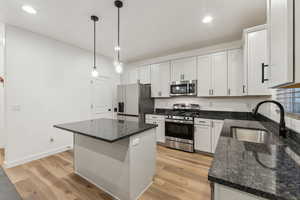 Kitchen with a kitchen island, sink, decorative light fixtures, white cabinetry, and appliances with stainless steel finishes