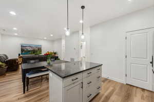 Kitchen featuring a kitchen island, white cabinetry, dark stone counters, light hardwood / wood-style flooring, and pendant lighting