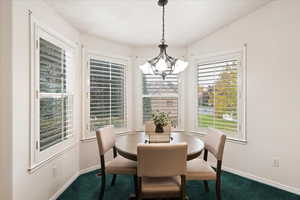 Dining space with a notable chandelier, lofted ceiling, and dark carpet