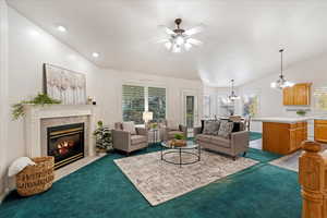 Carpeted living room featuring lofted ceiling, a high end fireplace, and ceiling fan with notable chandelier