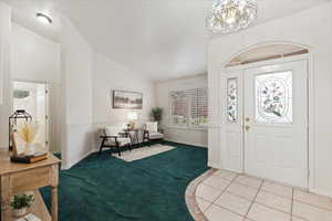 Carpeted foyer featuring lofted ceiling and a notable chandelier