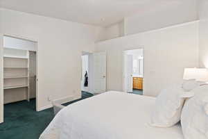 Carpeted bedroom with a spacious closet, ensuite bath, a closet, and a high ceiling