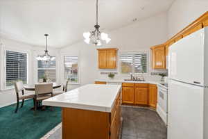 Kitchen with a kitchen island, vaulted ceiling, decorative light fixtures, sink, and white appliances