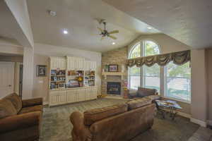 Living room featuring a stone fireplace, hardwood / wood-style floors, ceiling fan, and vaulted ceiling