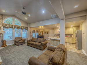 Living room featuring vaulted ceiling, light carpet, a fireplace, and ceiling fan with notable chandelier