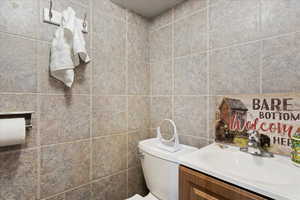 Bathroom featuring vanity, toilet, and tile walls