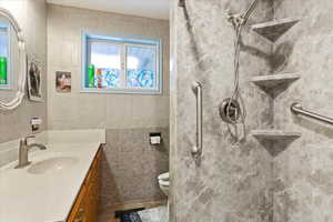 Recently remodeled Bathroom featuring vanity, toilet, tile walls, and an easy access shower.