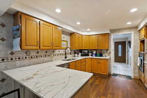 Kitchen featuring kitchen peninsula, stainless steel appliances, sink, light Dekton counters, and dark hardwood / wood-style flooring