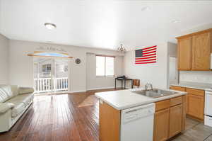 Kitchen featuring wood-type flooring, a center island with sink, sink, an inviting chandelier, and white appliances