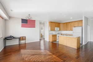 Kitchen with a center island with sink, dark hardwood / wood-style flooring, a chandelier, sink, and white appliances