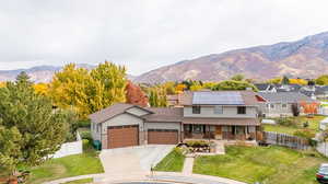 View of front of property featuring solar panels, covered porch, large 6 car garage, front yard, and mountain views