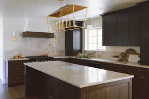 Kitchen with dark wood-type flooring, sink, tasteful backsplash, dark brown cabinets, and extractor fan