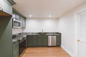 Kitchen with appliances with stainless steel finishes, light hardwood / wood-style flooring, dark stone countertops, and sink