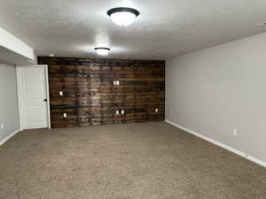 Basement featuring carpet floors, a textured ceiling, and wooden walls