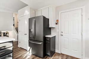 Kitchen with white cabinetry, stainless steel fridge, and dark hardwood / wood-style flooring