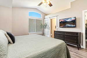 Bedroom with lofted ceiling, a barn door, light wood-type flooring, and ceiling fan