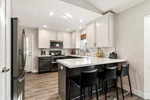 Kitchen with a breakfast bar area, hardwood / wood-style floors, appliances with stainless steel finishes, and white cabinetry