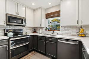 Kitchen featuring white cabinets, light stone counters, backsplash, sink, and stainless steel appliances