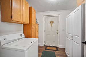 Washroom featuring washer / dryer, cabinets, a textured ceiling, dark wood-type flooring, and crown molding