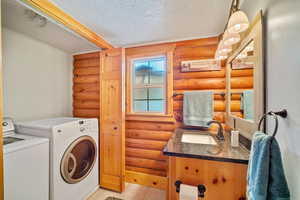 Laundry room with washing machine and dryer, sink, a textured ceiling, light tile patterned floors, and rustic walls