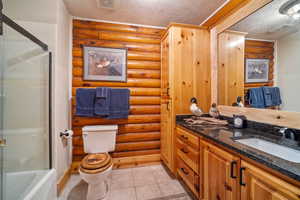 Full bathroom featuring enclosed tub / shower combo, a textured ceiling, toilet, vanity, and log walls