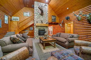 Living room featuring carpet, high vaulted ceiling, wooden ceiling, and a stone fireplace