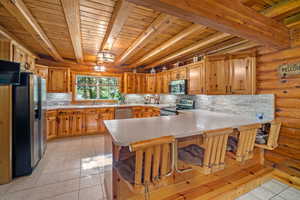 Kitchen with appliances with stainless steel finishes, kitchen peninsula, a kitchen breakfast bar, beam ceiling, and light tile patterned floors