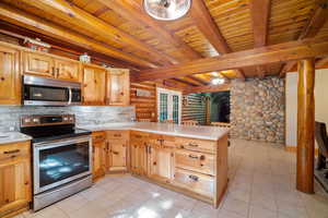 Kitchen featuring kitchen peninsula, wood ceiling, beam ceiling, light tile patterned floors, and appliances with stainless steel finishes