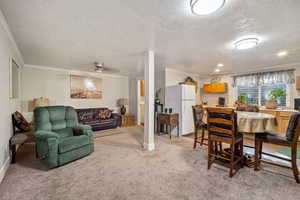 Carpeted living room featuring ornamental molding, a textured ceiling, and ceiling fan