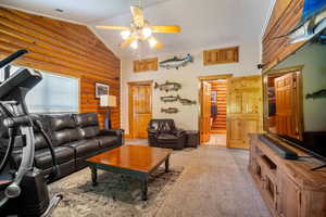 Living room with ceiling fan, light colored carpet, rustic walls, and vaulted ceiling