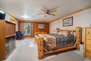 Carpeted bedroom with wood walls, ornamental molding, a textured ceiling, and ceiling fan