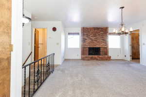 Unfurnished living room featuring a chandelier, light colored carpet, and a brick fireplace