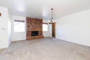 Unfurnished living room with an inviting chandelier, carpet flooring, and a fireplace