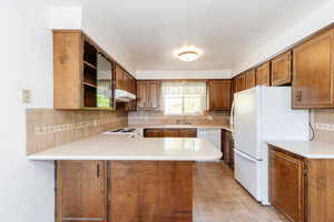 Kitchen with decorative backsplash, kitchen peninsula, sink, light tile patterned floors, and white appliances