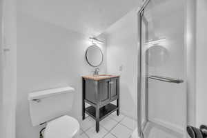 Bathroom with tile patterned floors, toilet, vanity, a textured ceiling, and an enclosed shower