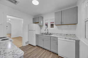 Kitchen with backsplash, wood-type flooring, gray cabinets, sink, and white appliances