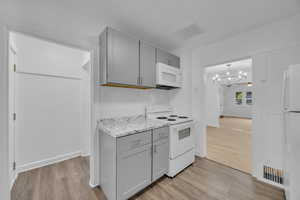 Kitchen featuring white appliances, gray cabinetry, backsplash, a notable chandelier, and light hardwood / wood-style flooring