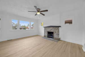 Unfurnished living room with a fireplace, a textured ceiling, light hardwood / wood-style floors, ceiling fan, and ornamental molding