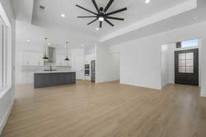 Unfurnished living room with light hardwood / wood-style floors, a raised ceiling, and ceiling fan