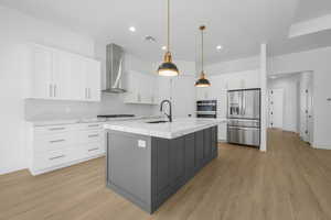 Kitchen featuring wall chimney range hood, an island with sink, sink, white cabinetry, and appliances with stainless steel finishes