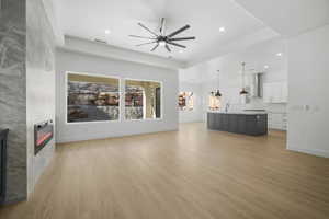 Unfurnished living room with a tiled fireplace, a raised ceiling, light hardwood / wood-style flooring, and ceiling fan